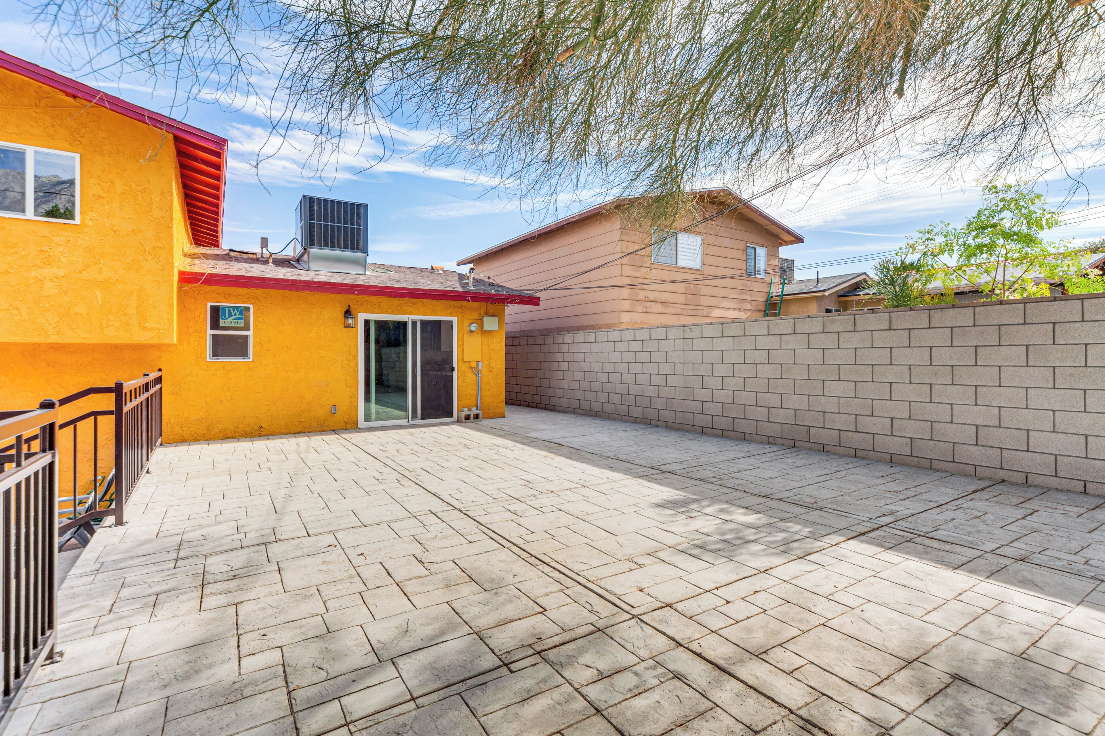A backyard with a paved patio, a brick wall, and a yellow building with a red roof.
