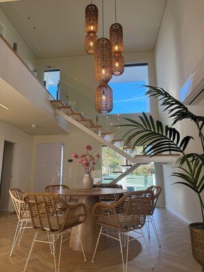 Un intérieur moderne comprenant un coin repas, des chaises en osier, une table ronde et un escalier.
