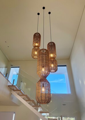 Un intérieur moderne agrémenté d’un escalier, de grandes fenêtres et d’un luminaire suspendu original.