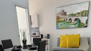 Een moderne woonkamer met een eethoek, een grijze bank met gele kussens, en een schilderij van een brug aan de muur.