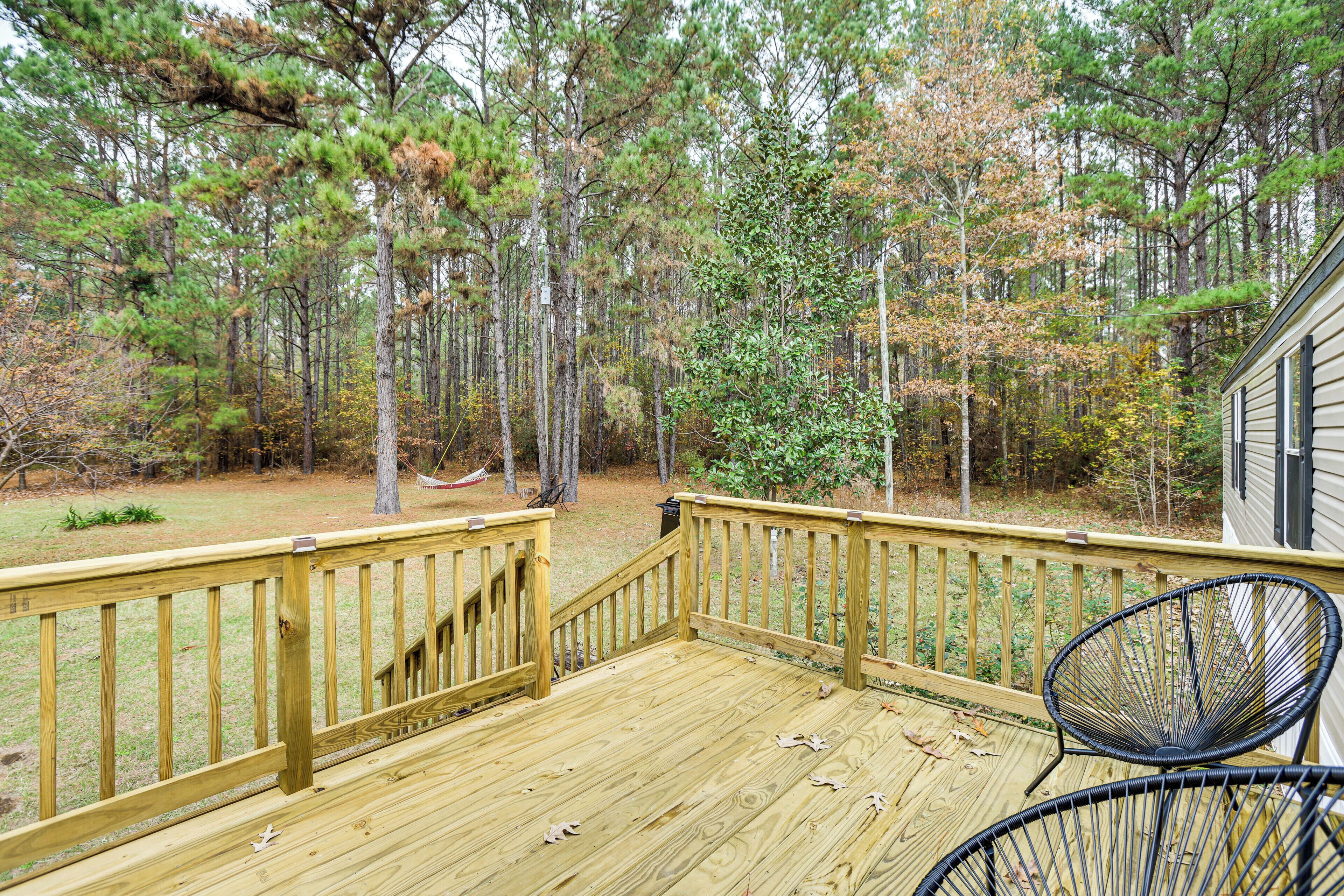 A wooden deck with a railing, surrounded by trees and a house.