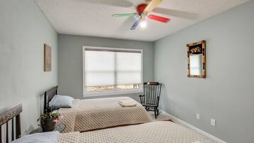 A bedroom with two beds, a ceiling fan, a window with blinds, a chair, and a mirror on the wall.