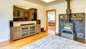 Ein Wohnzimmer mit Kamin aus Stein, Holzboden, einem großen Flachbildfernseher und einem Essbereich, der durch einen offenen Durchgang sichtbar ist.