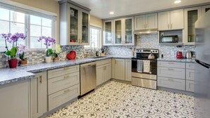 A modern kitchen with light-colored cabinets, a tiled backsplash, and a patterned floor. - Easy SF Access! Spacious Family Home w/ Yard (Daly City)