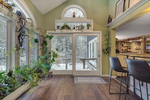 A spacious room with a large sliding glass door leading to a deck, wooden flooring, and a kitchen area with bar stools.