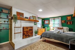 A bedroom with a white brick fireplace, green walls, a bed with a gray blanket, and a wooden dresser.
