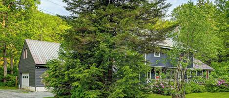 A house with a gravel driveway, a garage, and a large tree in the front yard.