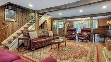 A spacious living room with a wooden staircase, leather furniture, and a large rug.