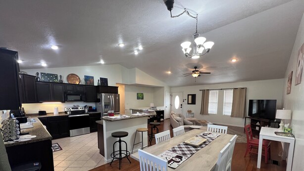 A spacious living area with a dining table, white chairs, a kitchen with dark cabinets, a refrigerator, and a ceiling fan. - Big Home right off I44 near Fort Leonard Wood (Saint Robert)
