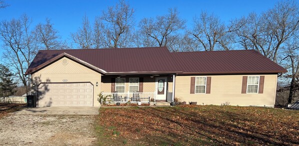 A single-story house with a brown metal roof, beige siding, and a front porch with a white railing. - Big Home right off I44 near Fort Leonard Wood (Saint Robert)
