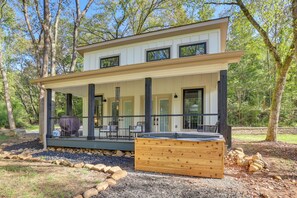 Una casa moderna de dos pisos con porche cubierto, mobiliario de exterior y un jacuzzi.