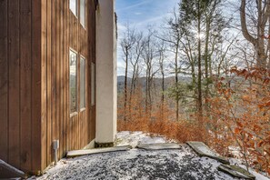 A wooden cabin with a stone pathway leading to a door, surrounded by autumn foliage and a snowy ground.