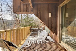 A wooden deck with a table and chairs, a glass door, and a view of trees and mountains.