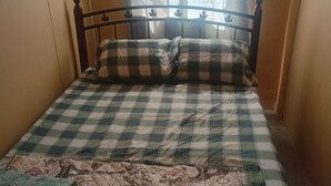 Una cama con colcha a cuadros y edredón floral, un cabecero de metal y una ventana con celosía decorativa.