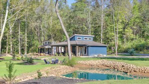 A house with a pond, surrounded by trees and a stone wall. - Waterfront 'Blue Spruce' Small Home in Wildwood! (Wildwood)