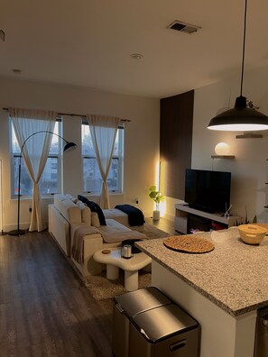 Een moderne woonkamer met een bank, een salontafel, een televisie en een keukenhoek met een aanrecht.