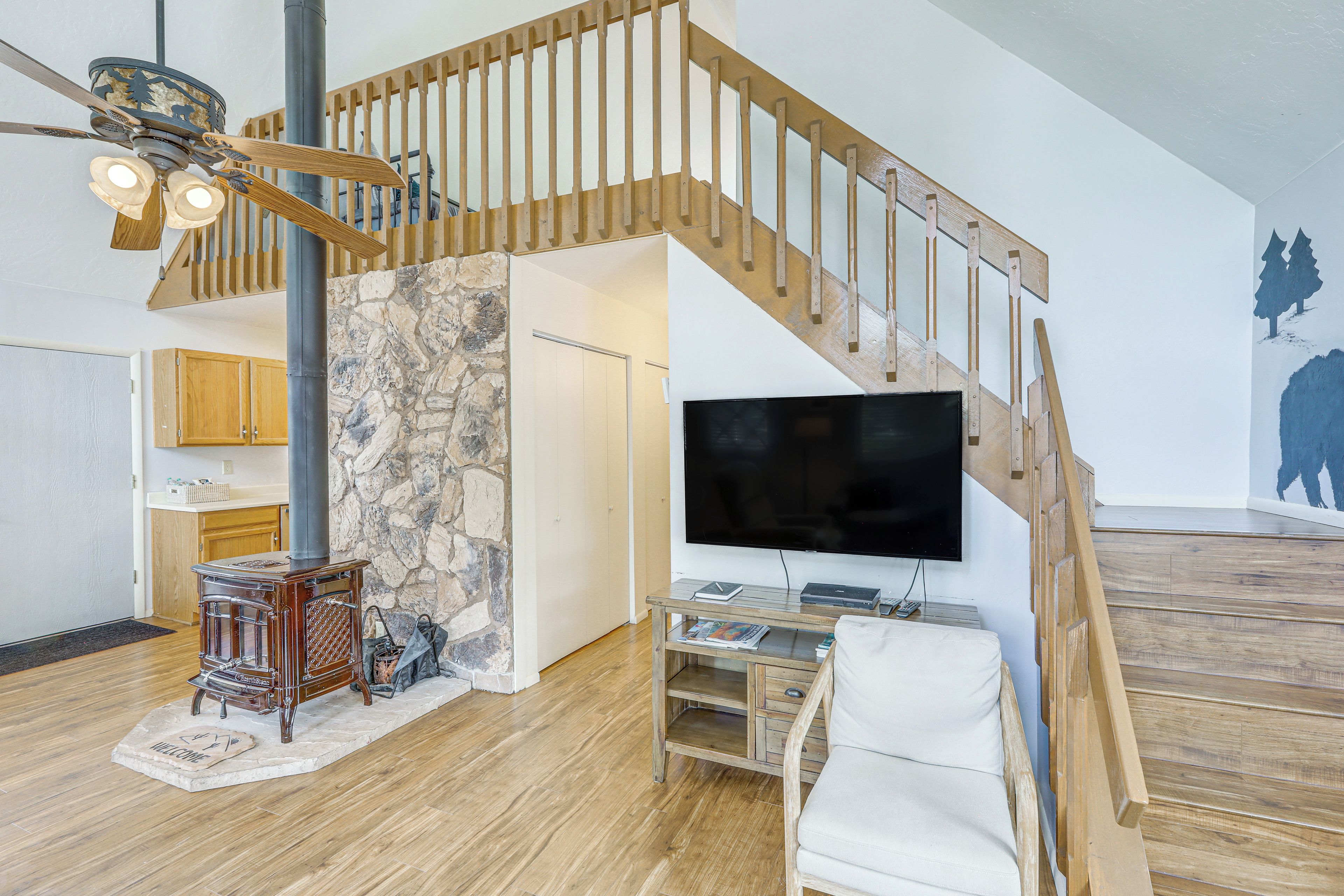 A modern living room with a wooden staircase, a stone wall, a fireplace, and a flat-screen TV.
