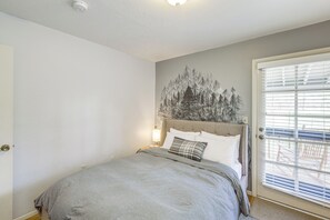 Ett sovrum med en säng, en sänggavel, en vägglampa och en dörr med persienner.