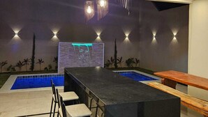 Zona de bar moderna con piscina, taburetes y un banco de madera.
