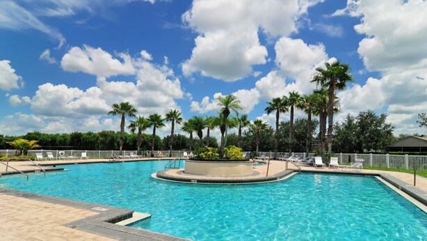 A swimming pool with clear blue water, surrounded by palm trees and lounge chairs, under a partly cloudy sky. - Peaceful gated retreat/Waterfront/Clubhouse (Bradenton)