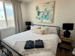 Une chambre à coucher avec un lit, deux tables de chevet, une fenêtre avec des rideaux et un tableau au mur.