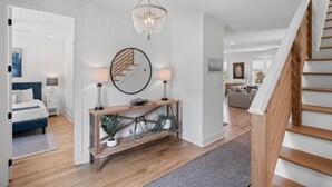 A modern living room with a staircase, a chandelier, a console table with decorative items, and a large mirror. - Walk to Beach | Private Pool | Close to Shops (Santa Rosa Beach)