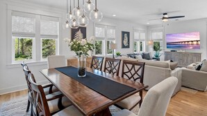 A spacious living room with a large TV, a dining area with a wooden table and chairs, and a ceiling fan. - Walk to Beach | Private Pool | Close to Shops (Santa Rosa Beach)