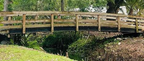 A wooden bridge over a stream in a park with trees and grass.