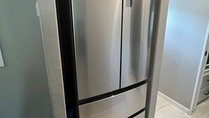 Ein Edelstahl-Kühlschrank in einer Küche mit hellgrauen Wänden und Holzboden.