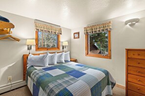 A bedroom with a bed, two bedside lamps, a dresser, and windows with curtains. - Glorious, dog friendly, 2 bedroom cabin with great views close to RMNP! (Estes Park)