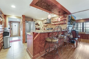 Eine Küche mit einer Holztheke, Barhocker, einem Kühlschrank und einer dekorativen Decke.
