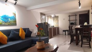 A living room with a blue sofa, wooden coffee table, and a painting of a tropical landscape. - El Rosal Cabin (Filandia)