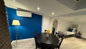 Quarto moderno com mesa de jantar, cadeiras, luminária, cama e ar-condicionado.