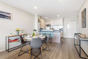 A modern kitchen with white cabinets, a central island, and a dining area with a round table and chairs. - Sky High Melbourne Views - Pool|Gym|Free Parking (Southbank)