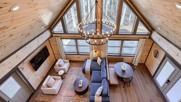 A spacious loft-style room with a large window, a chandelier, a sofa set, and a dining table.