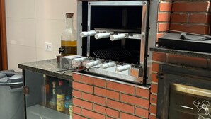 Cocina exterior de ladrillo con chimenea, encimera con botellas y horno de pizza.