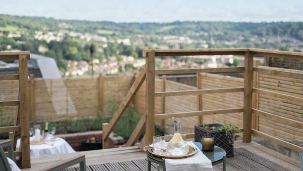 A wooden deck with a table set for dining, overlooking a town. - Garden apartment with balcony (Bath)