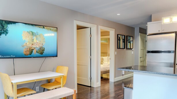 Eine moderne Küche mit integriertem Kühlschrank, einem Essbereich mit einer Bank und einem an der Wand befestigten Fernseher, der eine Naturlandschaft zeigt.