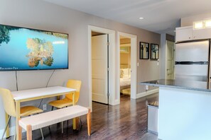Een moderne keuken met een ingebouwde koelkast, een eethoek met een bank, en een aan de muur bevestigde televisie waarop een natuurscène te zien is.