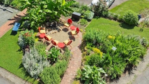 A circular outdoor seating area with red and yellow chairs, surrounded by a variety of plants and a paved walkway. - The Mountain View Cottage at Blue Ridge Hideaways (Weaverville)