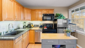 A compact kitchen with wooden cabinets, a stainless steel refrigerator, a microwave, a stove, and a sink. - The Mountain View Cottage at Blue Ridge Hideaways (Weaverville)
