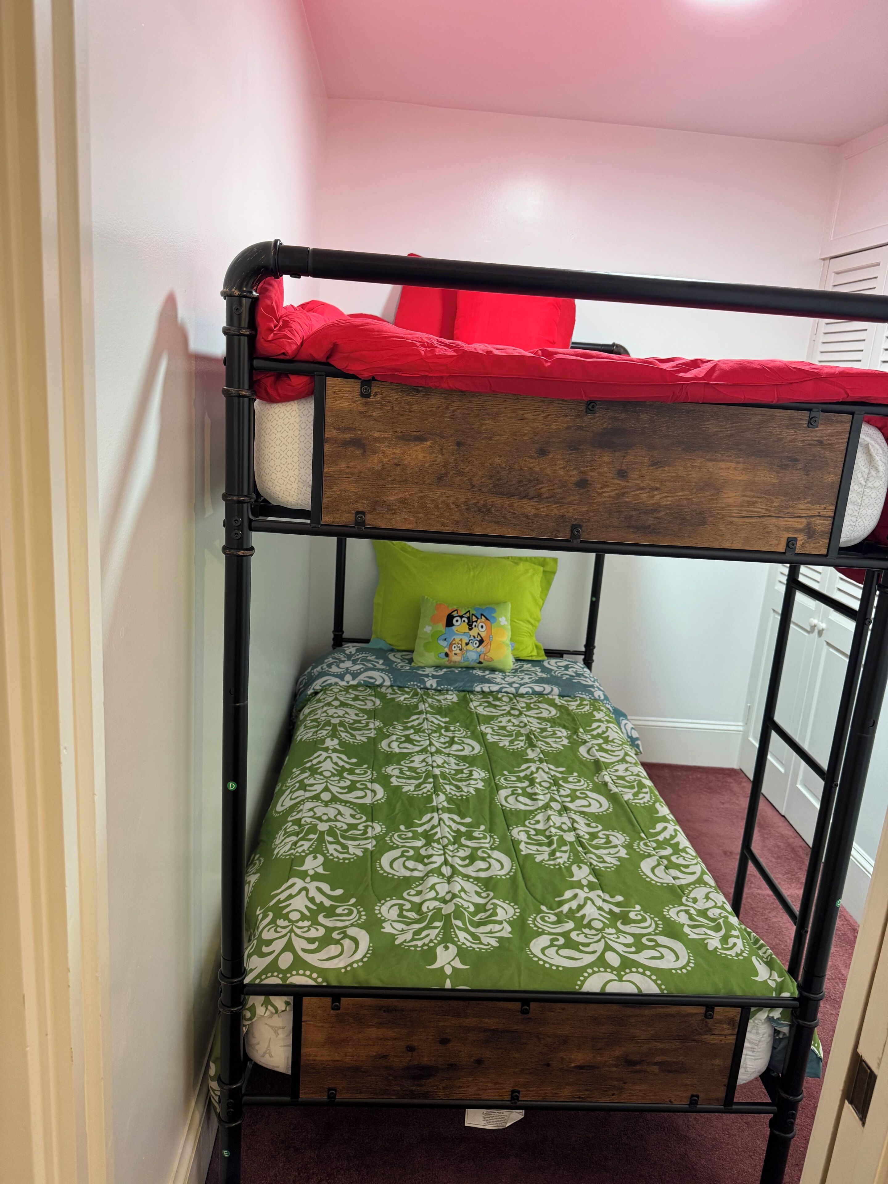 Una cama litera con un edredón estampado en verde, una cama superior roja y una almohada verde.