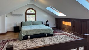 A bedroom with a skylight, a large bed, a nightstand, a dresser, and a window. - Experience comfort in our Danvers, MA 3-bedroom  (Danvers)