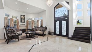 A spacious living room with ornate furniture, a large chandelier, and a grand staircase leading to an upper level. - Luxury Mediterranean Villa w/ Pool - Sleeps 10 (Morgan Hill)