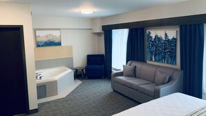 Habitación de hotel con cama, sofá, una mesita, sillón, bañera y obras de arte en las paredes.