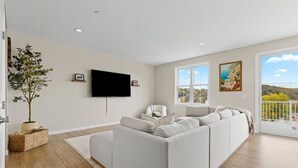 Ein modernes Wohnzimmer mit einer großzügigen Eckcouch, einem flachbildfernseher an der Wand und einem Balkon mit schöner Aussicht.