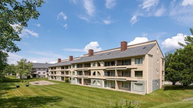 Een meerlaags hotel met een plat dak en meerdere schoorstenen, omgeven door verzorgde gazons en bomen.
