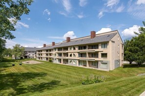 A multi-story hotel with a flat roof and multiple chimneys, surrounded by well-maintained lawns and trees. - Slopeside 2-Bedroom Condo w/ Fireplace & Kitchen (West Dover)