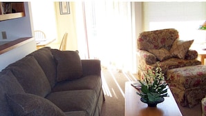 Een woonkamer met een bank, een bloemenarmstoel en een bijzettafeltje met een plant.