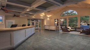 Eine geräumige Lobby mit einer Rezeption, einer Sitzecke und großen Fenstern mit Blick ins Freie.